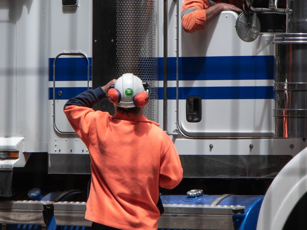 An instructor in high-visibility clothing speaking to a driver in a truck cab.